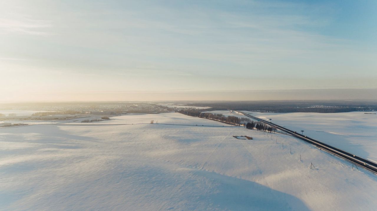 Vue aérienne d'une route droite traversant une plaine enneigée au lever du soleil