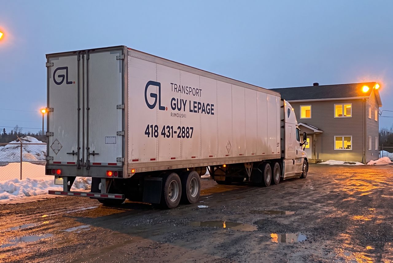 Remorque de Transport Guy Lepage vue de l'arrière dans une cour enneigée, bureau éclairé à la tombée de la nuit